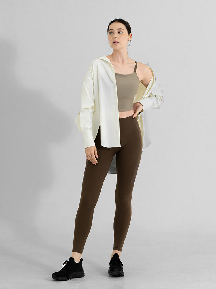 オーバーサイズシャツとブラトップを合わせた女性が、BEABLOOM(ビーブルーム)のブラウンレギンスを着用して立っている。ナチュラルで上品な印象を与えるヨガ・ピラティスウェアスタイル。