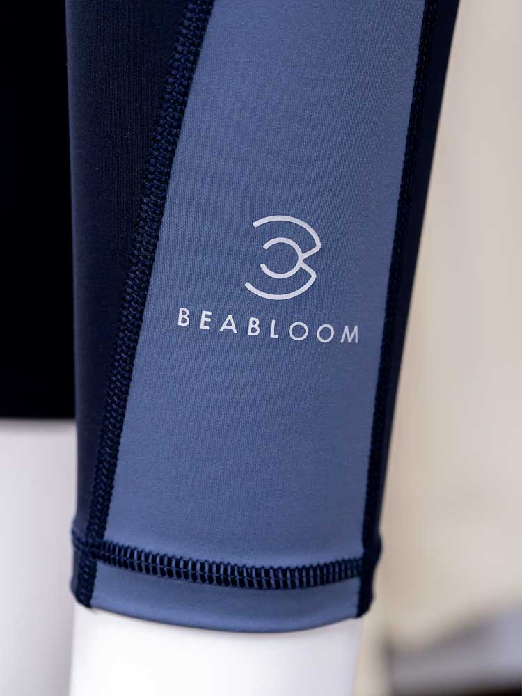 ヨガウェア・ピラティスウェアブランド『ビーブルーム(BEABLOOM)』のロゴがデザインされたブルーとネイビーの切り替えデザインレギンスのクローズアップ画像。高品質な素材とスタイリッシュなデザインで、快適さと機能性を兼ね備えたヨガやピラティスに最適なウェア。